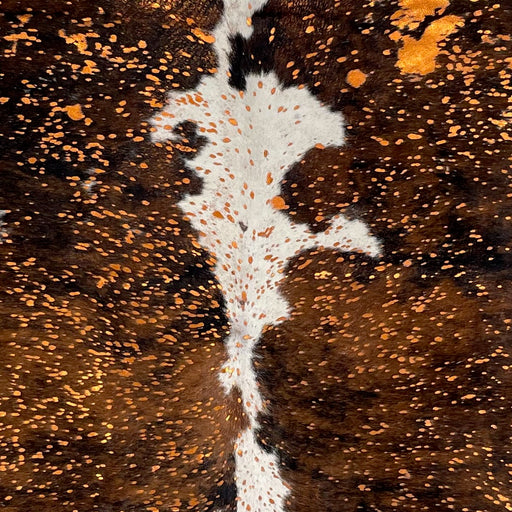 Closeup of this Colombian Tricolor Cowhide, showing white with spots that have a brown and black, brindle pattern, and a metallic, orange acid wash (COAW471)