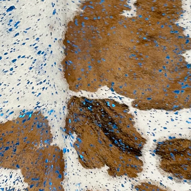 Closeup of this Large Tricolor Colombian Cowhide, showing white with large and small spots that have a brown, brindle pattern, and a sea blue, metallic acid wash (COAW484)