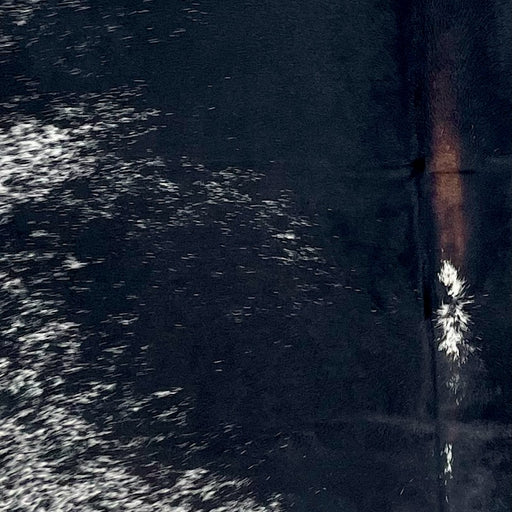Closeup of this XL Speckled Colombian Cowhide, showing white with black speckles and spots, mostly solid black down the middle, and dark brown down part of the spine (COSP3352)
