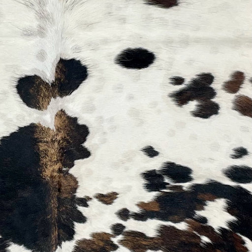 Closeup of this Large Colombian Tricolor Cowhide, showing white with large and small spots that have a mix of black and brown, and small, faint, brown spots down the middle (COTR1189)