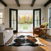 Tricolor cowhide rug CH-072 in a modern farmhouse living room with shiplap walls, black French doors to a porch, linen sofa and leather armchair