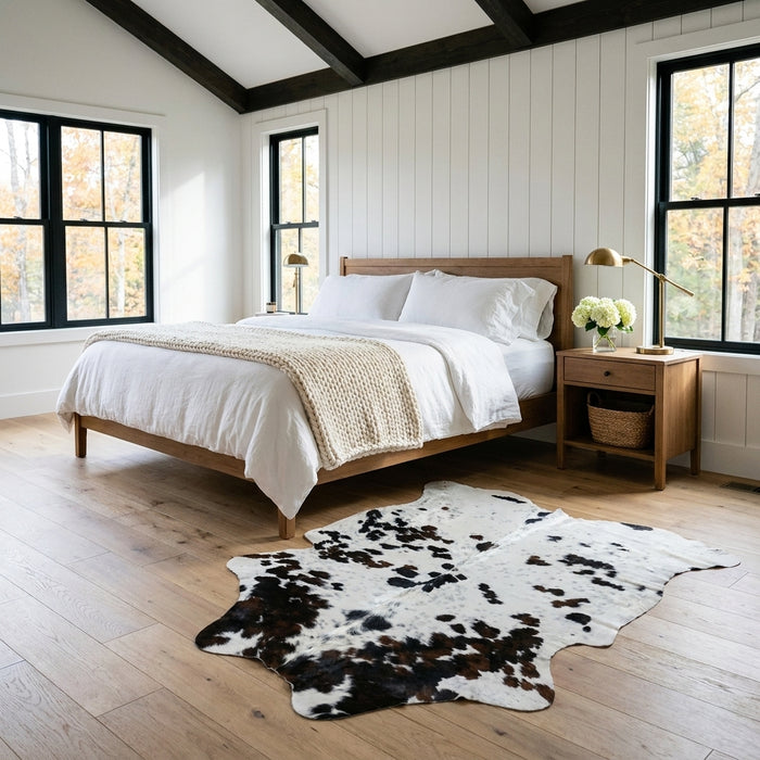 Tricolor cowhide rug CH-032 at the foot of a bed in a bright modern farmhouse bedroom with shiplap walls and white linen bedding