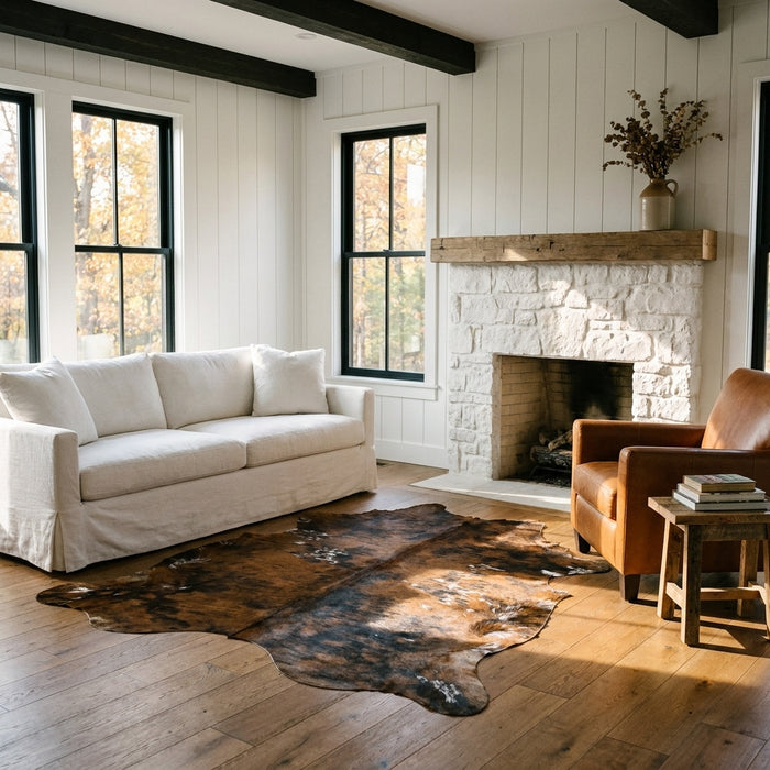 Tricolor cowhide rug CH-006 in a modern farmhouse living room by a whitewashed stone fireplace, with a linen sofa and leather armchair