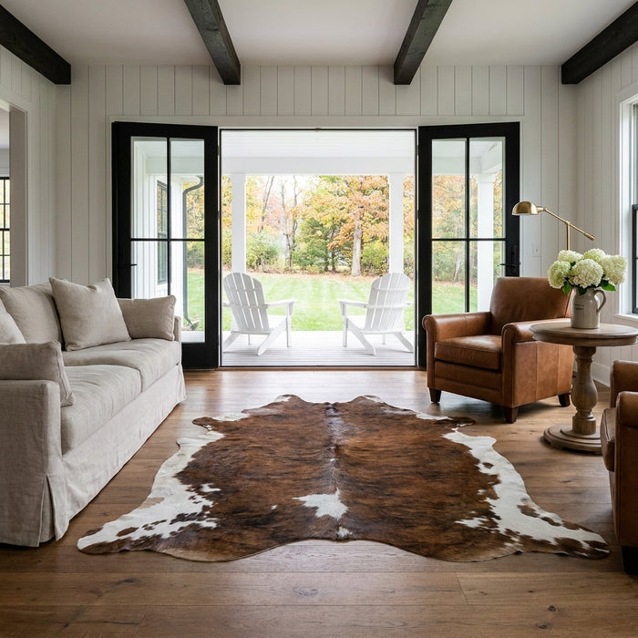 Tricolor cowhide rug CH-080 in a modern farmhouse living room with shiplap walls, black French doors to a porch, linen sofa and leather armchair