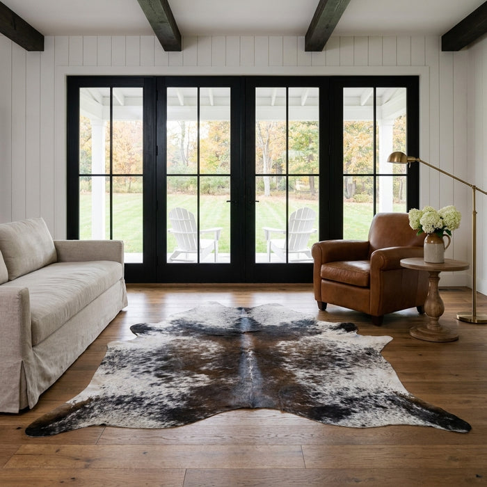 Grey and black salt and pepper cowhide rug in a modern farmhouse living room with black French doors, linen sofa and leather club chair