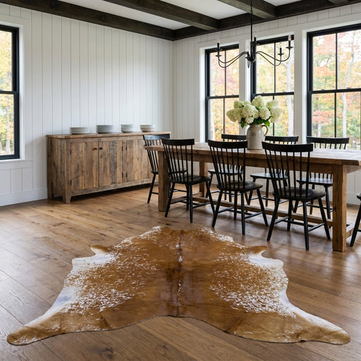 Brown salt and pepper cowhide rug on the oak floor of a modern farmhouse dining room with a rustic wood table and black Windsor chairs