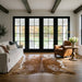 Brown salt and pepper cowhide rug in a modern farmhouse living room with black French doors, linen sofa and leather club chair