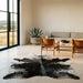 Dark salt and pepper Brazilian cowhide rug on a limestone floor in a minimal Texas Hill Country living room with leather sling chairs