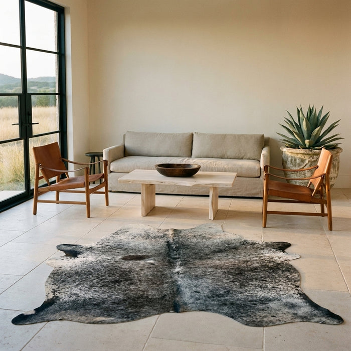 Dark salt and pepper Brazilian cowhide rug on a limestone floor in a minimal Texas Hill Country living room with leather sling chairs