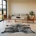 Dark salt and pepper Brazilian cowhide rug on a limestone floor in a minimal Texas Hill Country living room with leather sling chairs