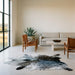 Dark salt and pepper Brazilian cowhide rug on a limestone floor in a minimal Texas Hill Country living room with leather sling chairs
