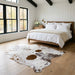 Brown and white salt and pepper cowhide rug at the foot of a bed in a bright modern farmhouse bedroom with light oak floors
